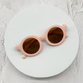 Load image into Gallery viewer, Soft blush pink round sunglasses with brown-tinted lenses, displayed on a minimalist white circular platform