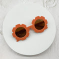 Load image into Gallery viewer, Round sunglasses with rust-coloured flower-shaped frames and brown lenses, displayed on a white circular surface.