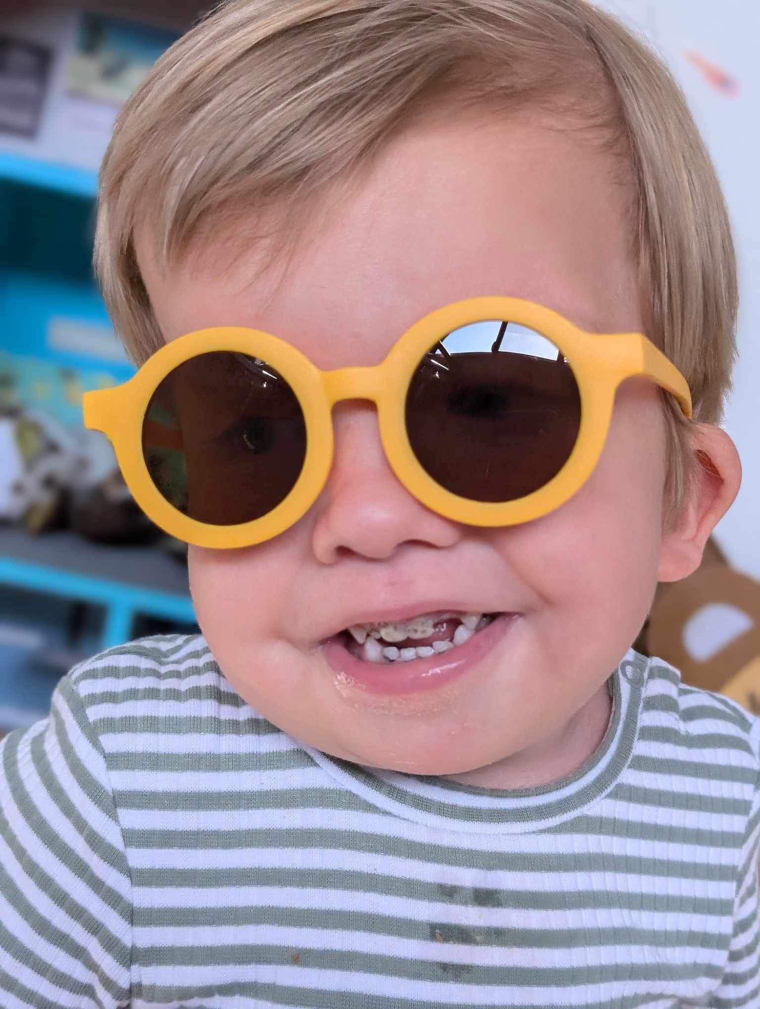 Happy toddler wearing yellow round sunglasses and a green-striped shirt.