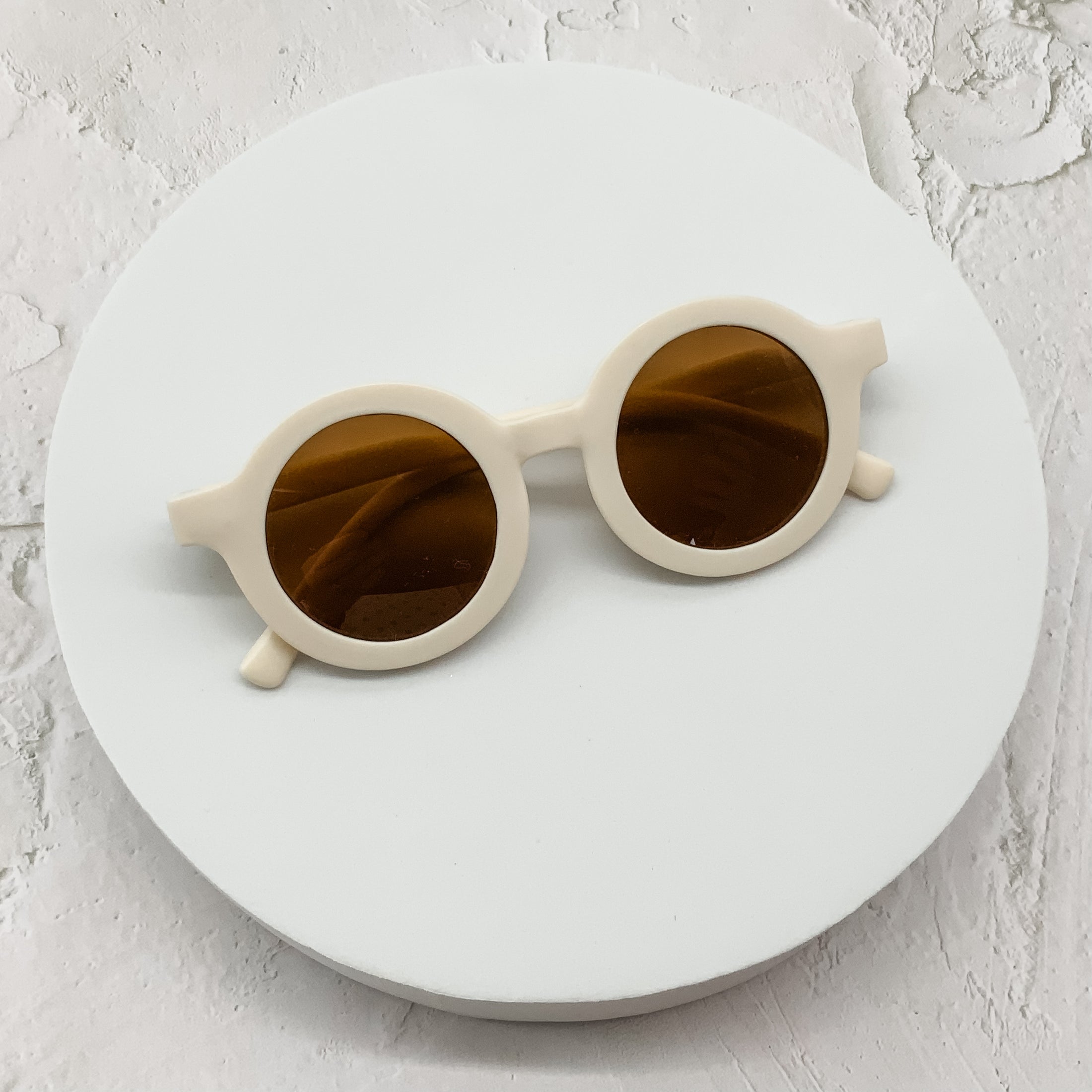 Off-white round sunglasses with brown-tinted lenses, showcased on a minimalistic white circular backdrop.