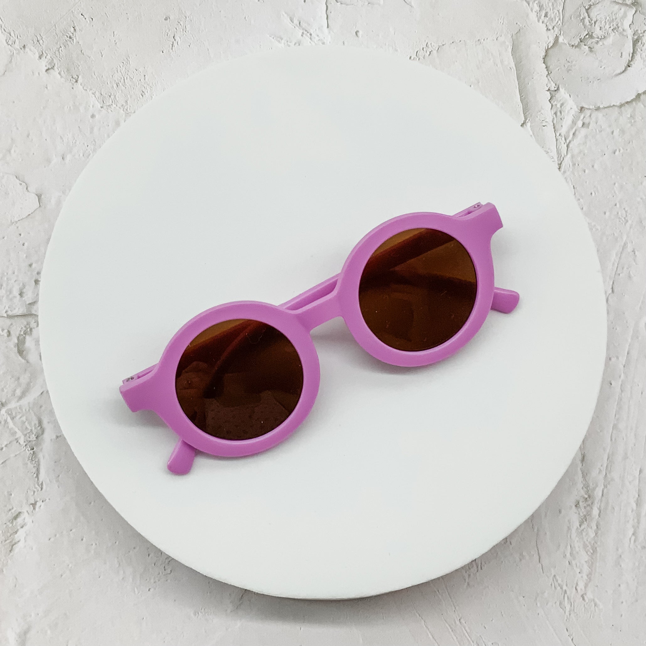Vibrant purple round sunglasses with brown-tinted lenses, displayed on a clean white circular platform.