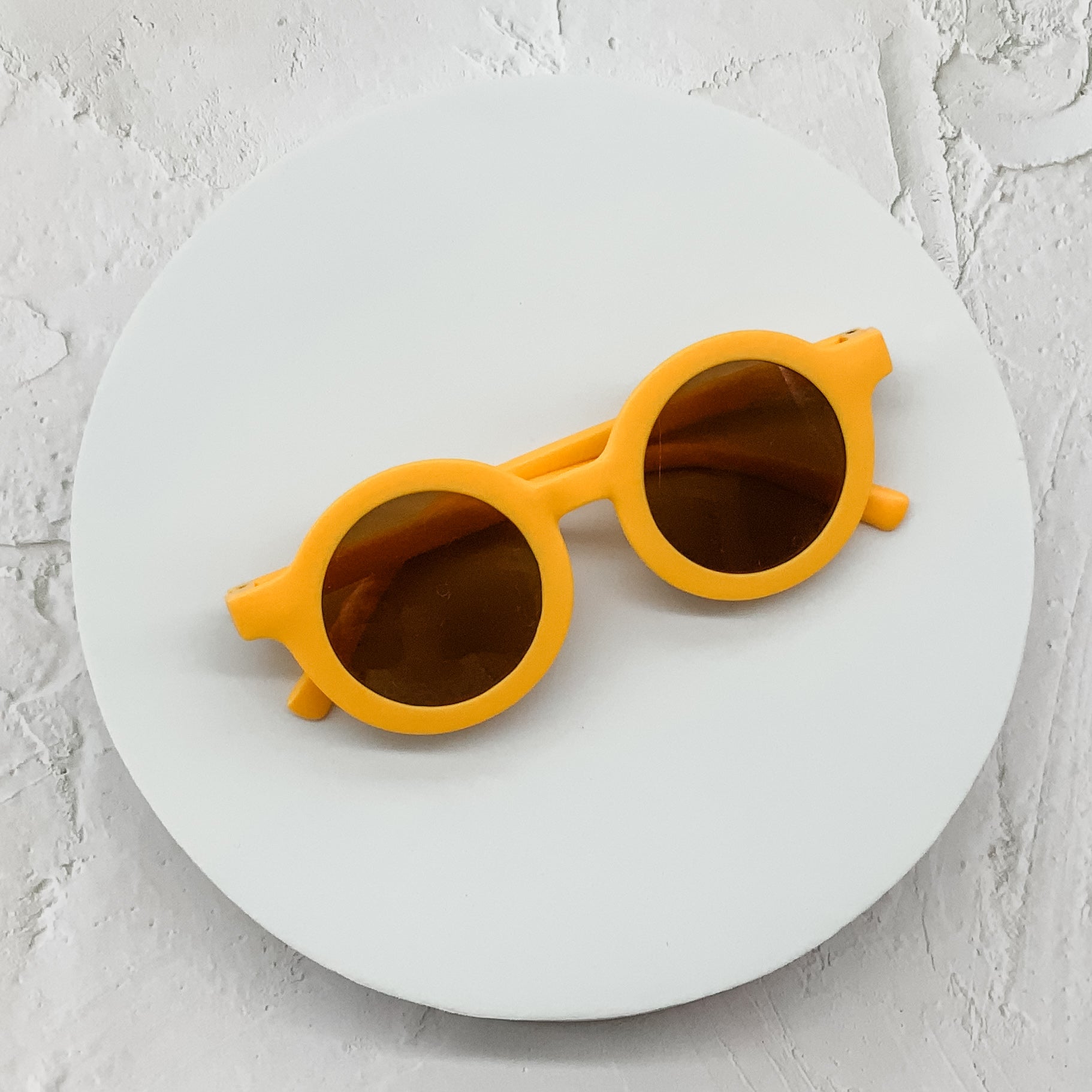 Round dark green sunglasses with brown lenses, elegantly placed on a minimalist white circular platform.