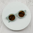 Load image into Gallery viewer, Round pastel green sunglasses with brown lenses, neatly displayed on a minimal white circular surface.
