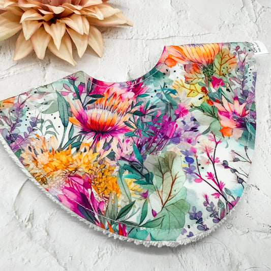 Floral Dribble Bib – Handmade baby bib featuring a vibrant Australian native floral print. Made with a soft cotton front and absorbent towelling backing. Stylish and practical for everyday use.